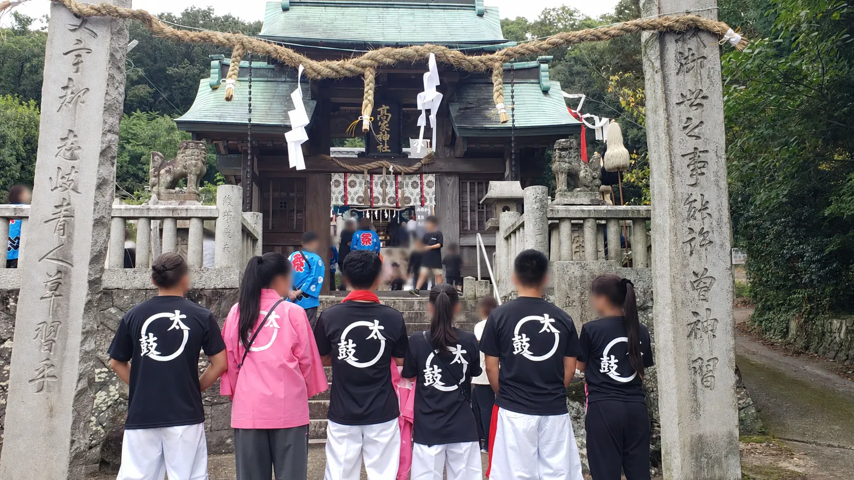 お祭り「揚太鼓台」の円＋太鼓ロゴ入りおそろいTシャツ（背面）を着て神社に参拝する着用イメージ